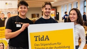 Drei junge Menschen halten ein Schild mit der Aufschrift TidA, das Stipendium für Talente in der Ausbildung