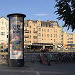Eine rotierende Werbesäule in der Berliner Straße in Tegel. Im Hintergrund fahren Autos, rechts sind Fahrräder abgestellt.