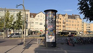 Eine rotierende Werbesäule in der Berliner Straße in Tegel. Im Hintergrund fahren Autos, rechts sind Fahrräder abgestellt.