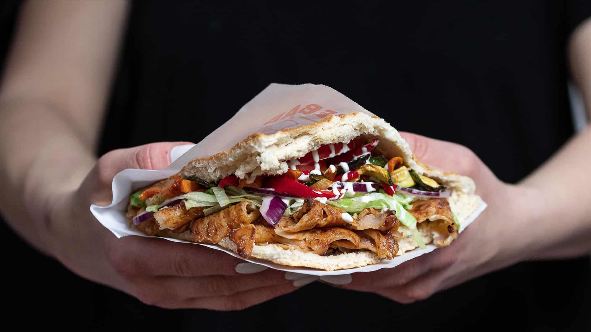 Zwei Hände halten einen gefüllten Döner im Fladenbrot