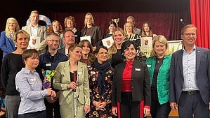 Eine große Gruppe von Frauen und Männern steht mit Urkunden nebeneinander für ein Gruppenbild vor einem roten Vorhang.