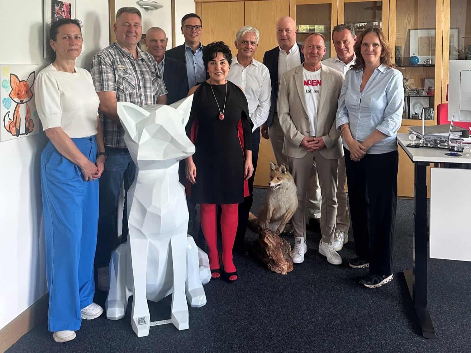 Elf Personen stehen für ein Gruppenbild in einem Büro des Bezirksamts Reinickendorf zusammen, vor ihnen eine weiße Fuchsskulptur.