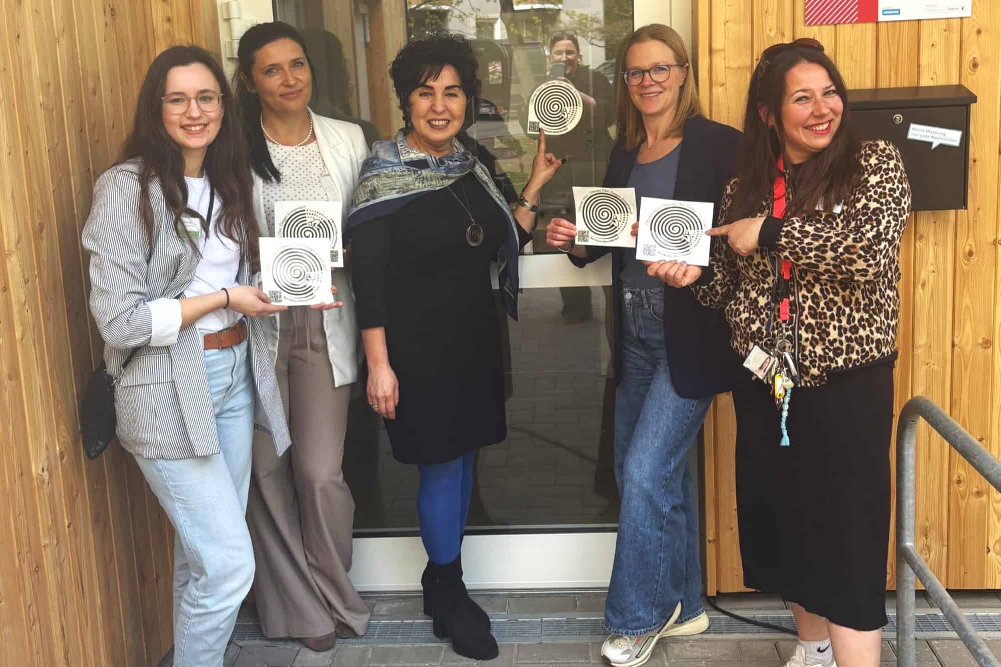 Fünf Frauen stehen vor dem Eingang des Kiezorts Brusi und halten Sticker der Einsamkeitskampagne hoch.