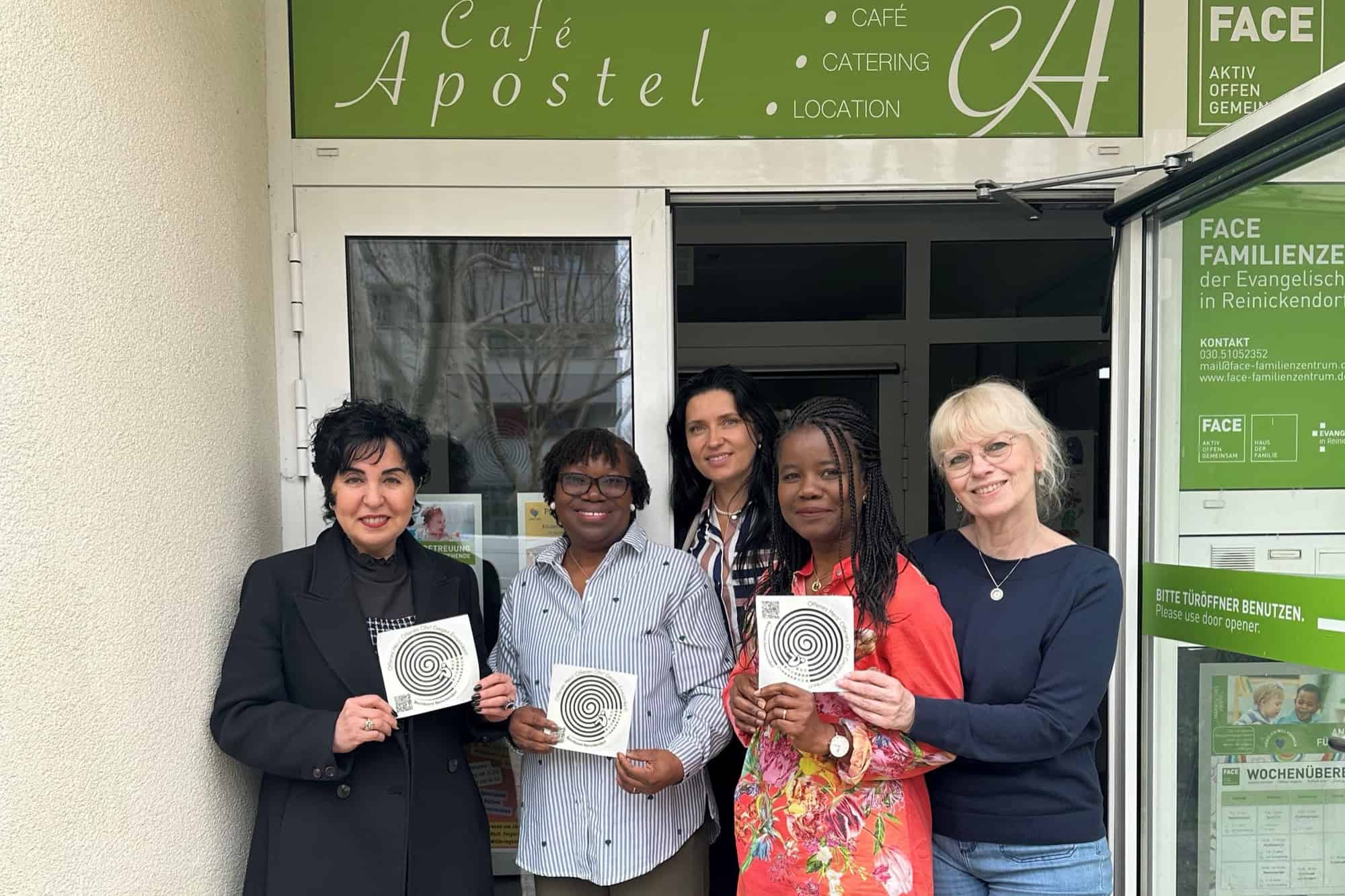 Fünf Frauen stehen vor dem Eingang des Café Apostel und halten Sticker der Einsamkeitskampagne hoch.