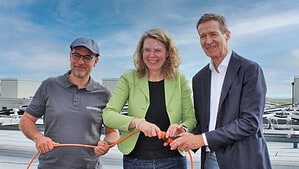 Drei Personen stehen auf einem Flachdach zwischen Solarmodulen und halten ein orangefarbenes Kabel.