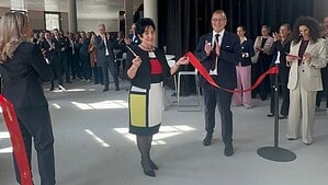 Eine Frau durchschneidet in einer hellen Halle mit Betondecke ein rotes Band, um sie herum applaudieren zahlreiche Gäste.