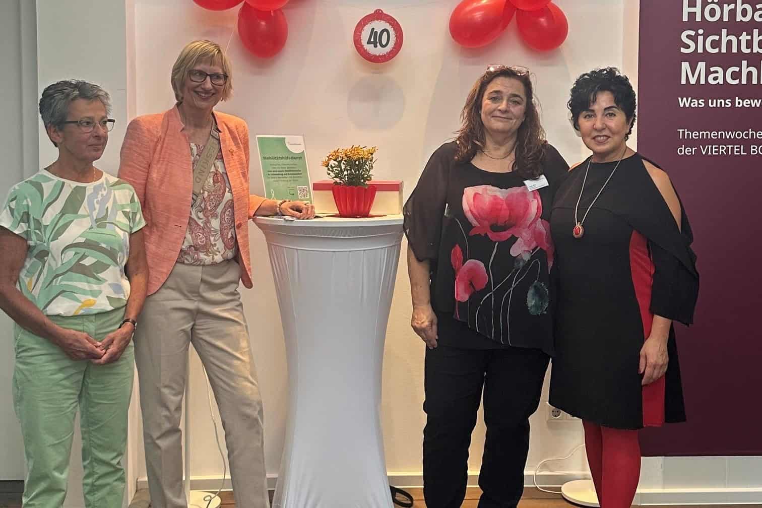 Vier Frauen stehen bei der Jubiläumsfeier des Mobilitätshilfedienstes vor roten Luftballons und einem Schild mit der Zahl 40.