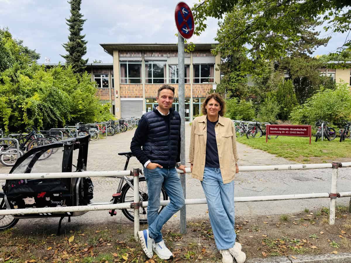 Ein Mann und eine Frau stehen am Geländer vor dem Eingang der Renée-Sintenis-Grundschule in Frohnau, daneben ein Halteverbotsschild