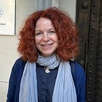 Eine Frau steht lächelnd neben einem Schild mit der Aufschrift Welcome am Portal der Dorfkirche Alt-Tegel