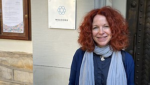Eine Frau steht lächelnd neben einem Schild mit der Aufschrift Welcome am Portal der Dorfkirche Alt-Tegel
