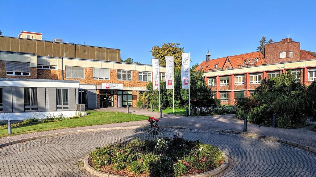 Eingangsbereich der Caritas-Klinik Dominikus mit Vorplatz, Blumenbeet und Fahnen