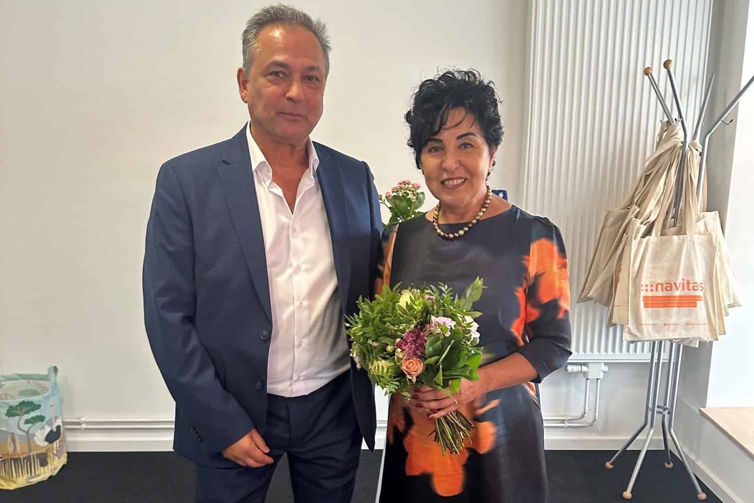 Ein Mann im dunklen Anzug und eine Frau mit Blumenstrauß stehen in den Räumen der neuen Beratungsstelle.