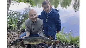 Ein Mann und ein Junge hocken am Ufer des Waldsees in Hermsdorf und halten einen großen Hecht in den Händen.