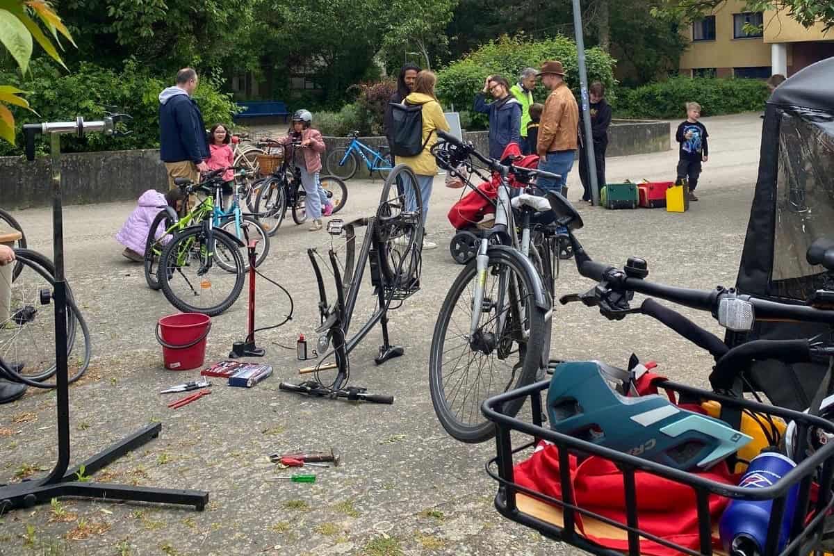 Werkzeug, Montageständer und Fahrräder an der Reparaturstation, dahinter Gäste im Gespräch
