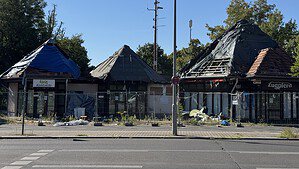 Drei ausgebrannte Pavillons mit Planen auf den Dächern hinter Bauzäunen an der Gorkistraße in Tegel