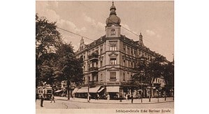 Historische Ansichtskarte in Sepia: großes Eckhaus mit Turmhaube, im Erdgeschoss Schaufenster mit dem Schriftzug Kaufhaus Tegel, davor Straßenbahn und Passanten, darunter die Zeile Schlieper-Straße Ecke Berliner Straße.
