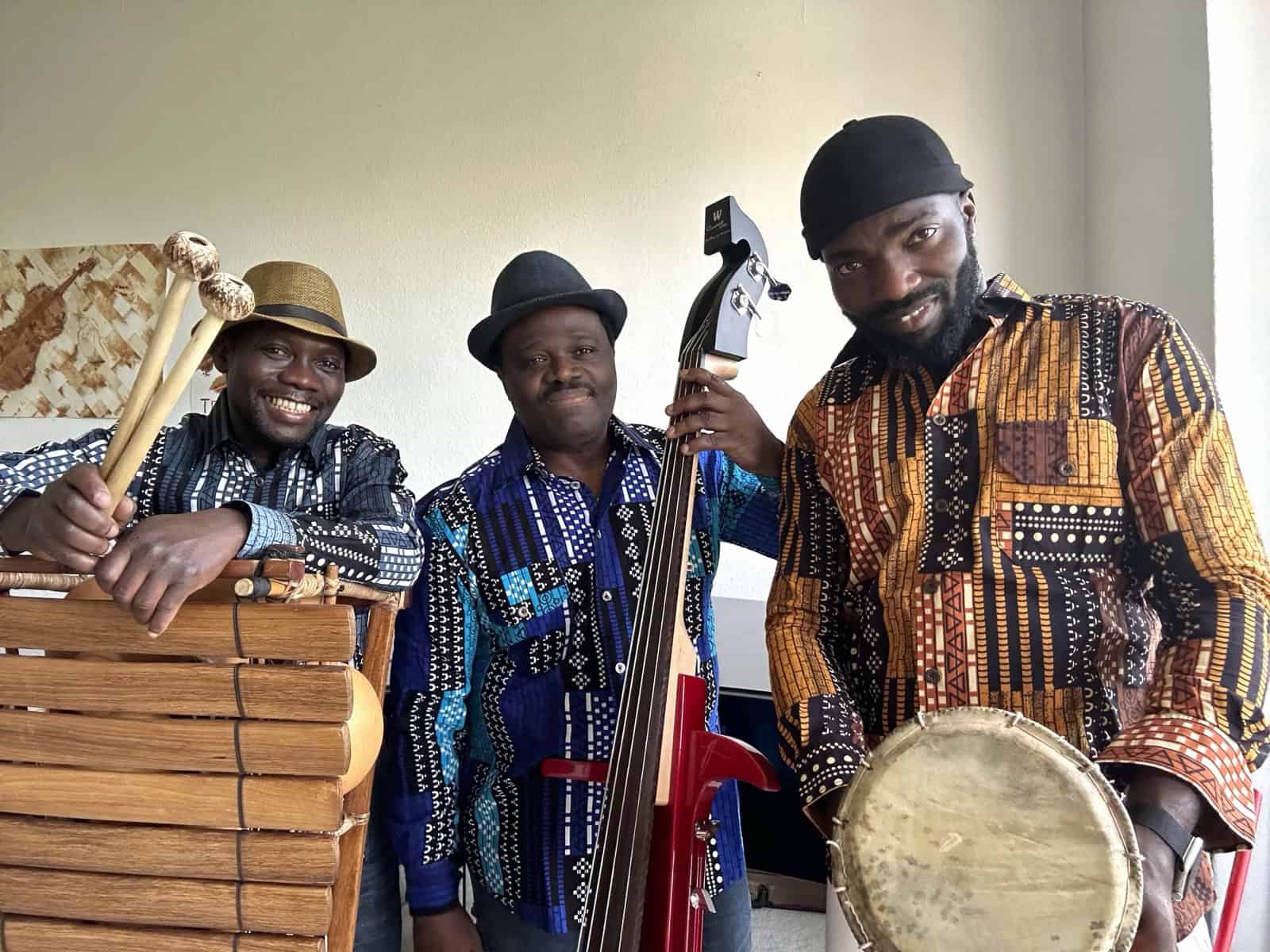 Drei Musiker in bunt gemusterten Hemden mit Balafon, E-Kontrabass und Trommel.