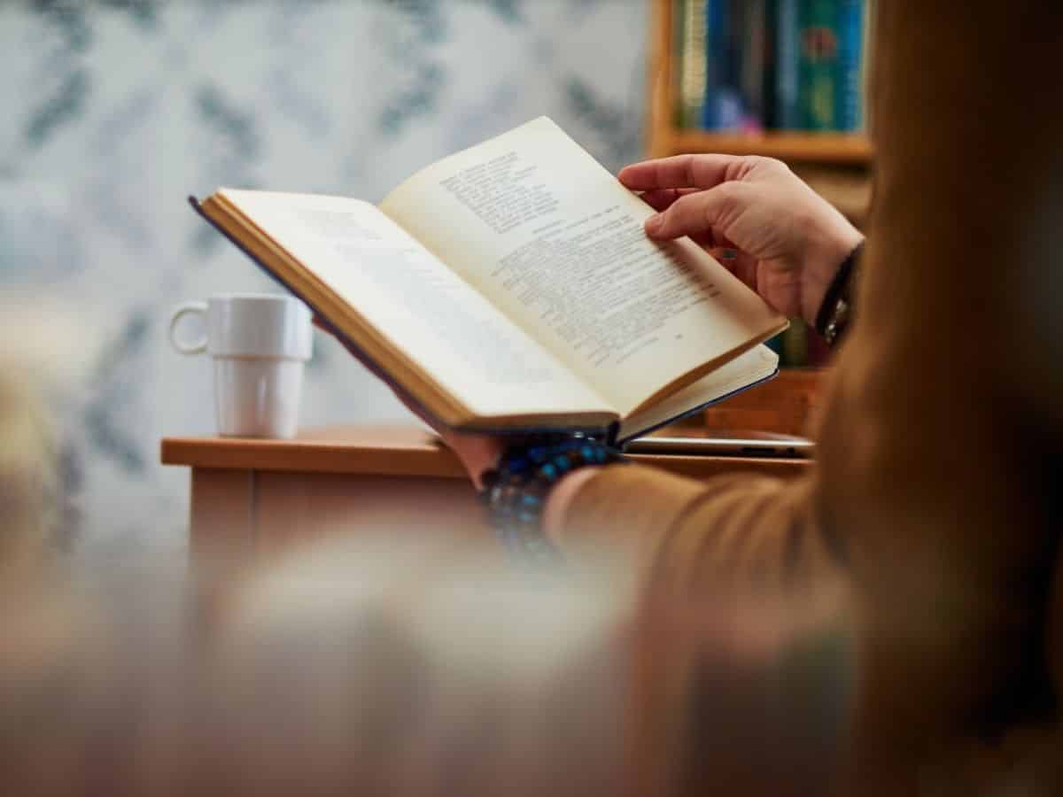 Eine Hand blättert in einem aufgeschlagenen Buch, daneben steht eine Tasse