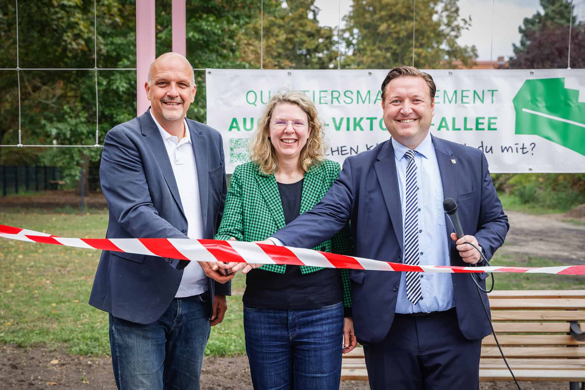 Zwei Männer und eine Frau zerschneiden ein rot-weißes Absperrband mit einer Schere.
