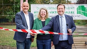 Zwei Männer und eine Frau zerschneiden ein rot-weißes Absperrband mit einer Schere.