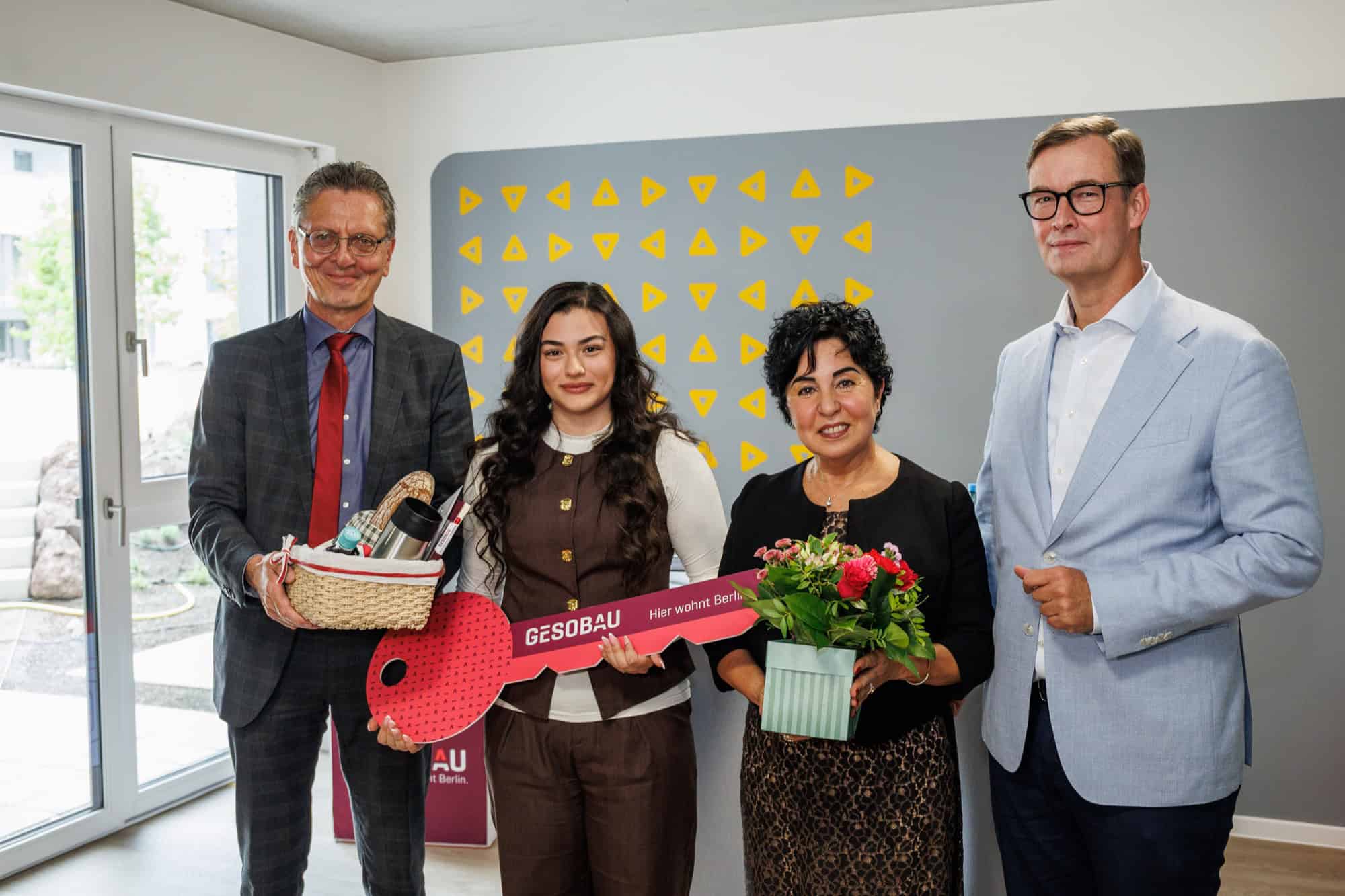 Vier Personen stehen in einem Wohnraum, eine junge Frau hält einen großen roten Schlüssel aus Pappe