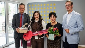 Vier Personen stehen in einem Wohnraum, eine junge Frau hält einen großen roten Schlüssel aus Pappe