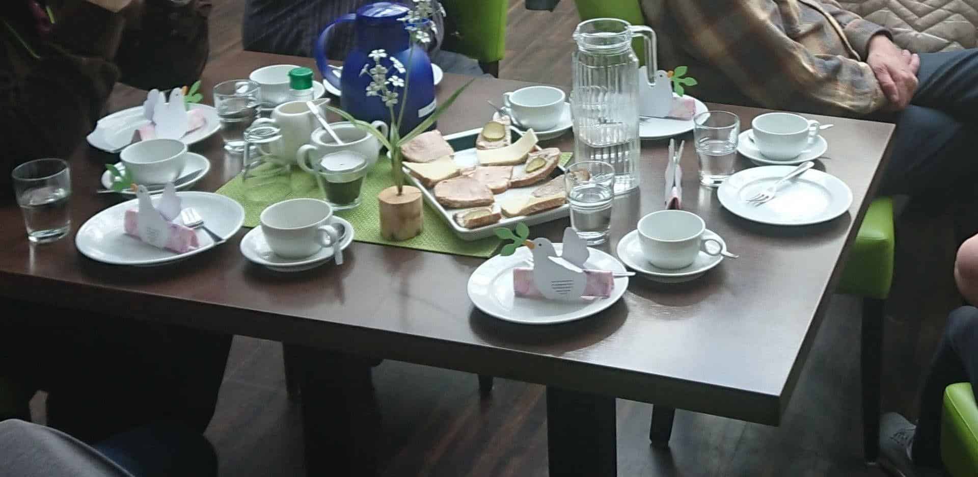 Gedeckter Kaffeetisch im Café Apostel mit Tassen, Karaffen, belegten Broten und Papiertauben als Tischschmuck