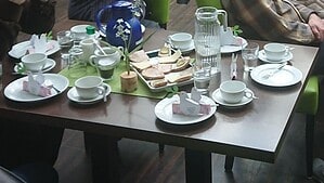 Gedeckter Kaffeetisch im Café Apostel mit Tassen, Karaffen, belegten Broten und Papiertauben als Tischschmuck