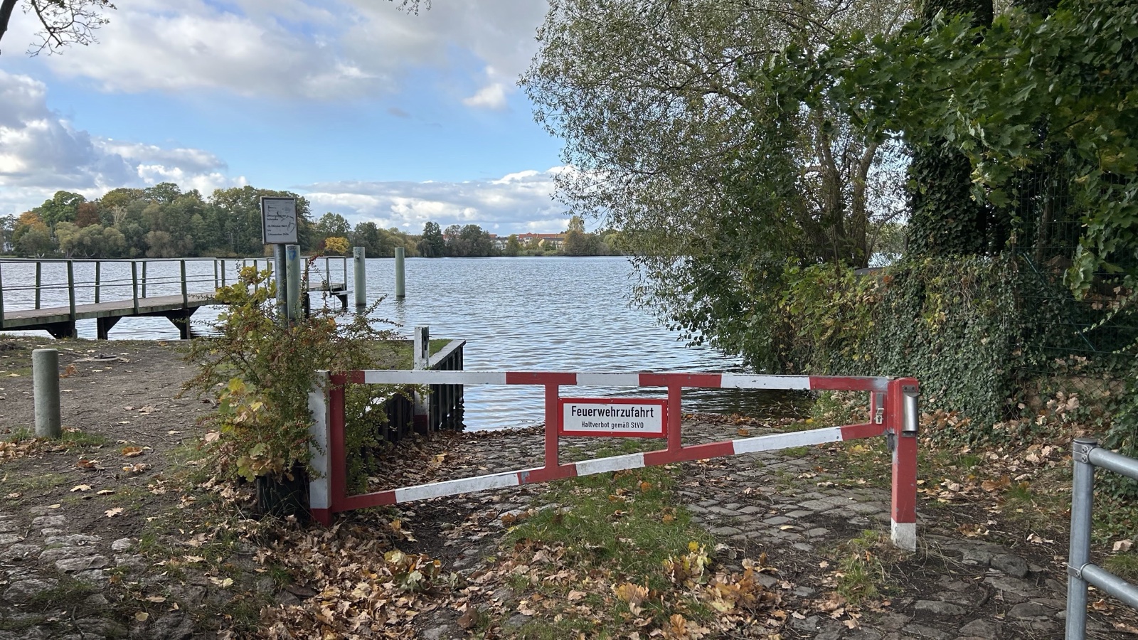 Slipanlage an der Fährstraße in Heiligensee: gepflasterte Rampe zum Wasser mit rot-weißer Schranke, links ein Steg