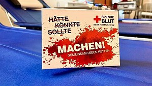 Werbekarte mit der Aufschrift Hätte, könnte, sollte, machen! auf einer blauen Blutspendeliege