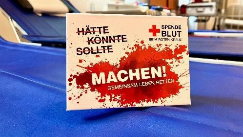 Werbekarte mit der Aufschrift Hätte, könnte, sollte, machen! auf einer blauen Blutspendeliege
