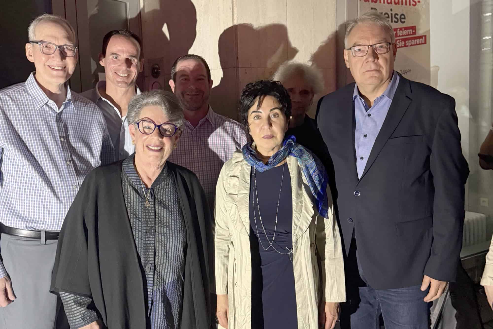Sieben Personen stehen am Abend vor einer hellen Hauswand