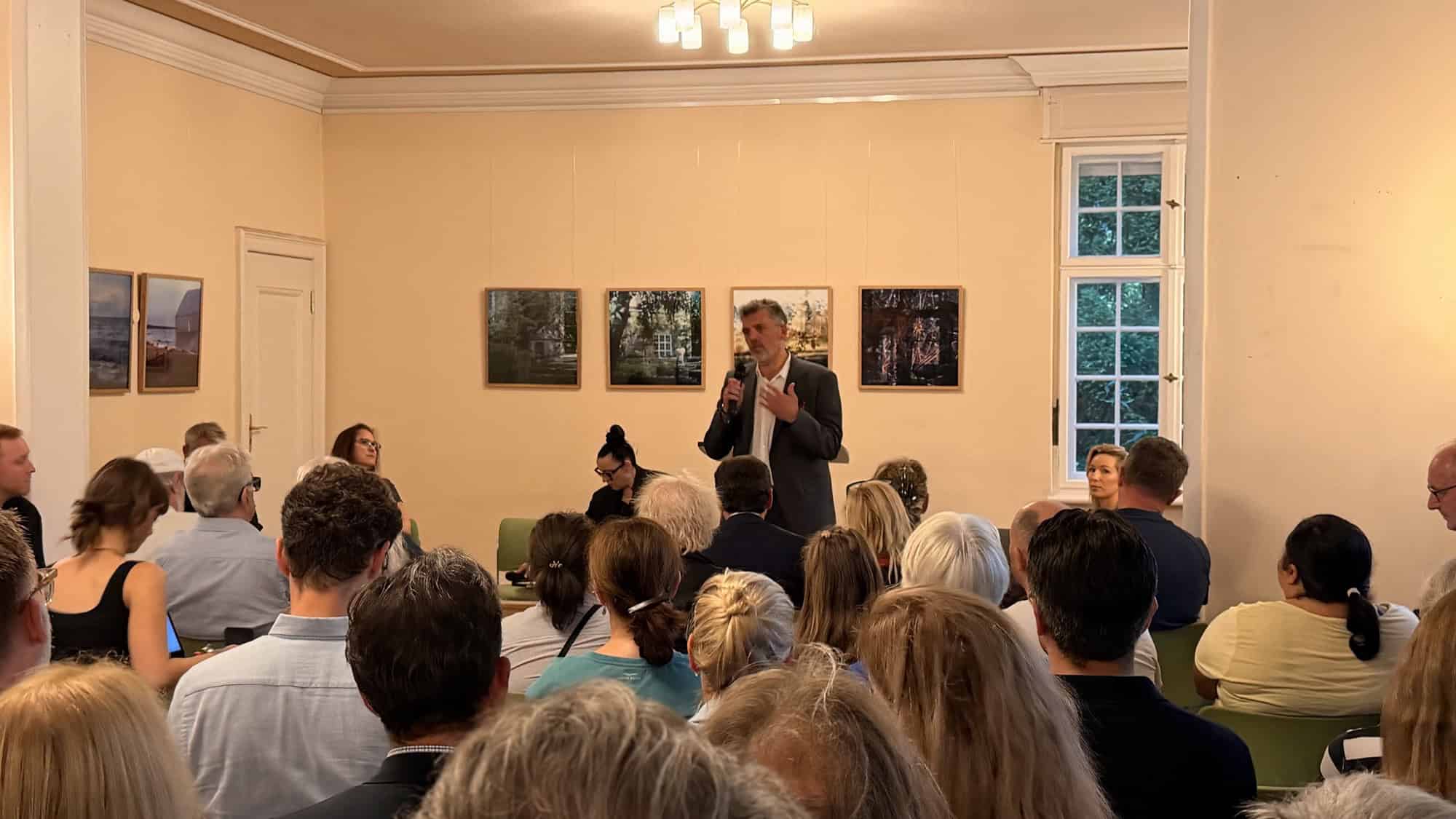 Ein Mann spricht mit Mikrofon vor einem voll besetzten Saal im Centre Bagatelle
