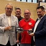 Vier Männer halten in der neuen Sporthalle gemeinsam einen übergroßen symbolischen Schlüssel.