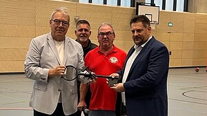 Vier Männer halten in der neuen Sporthalle gemeinsam einen übergroßen symbolischen Schlüssel.