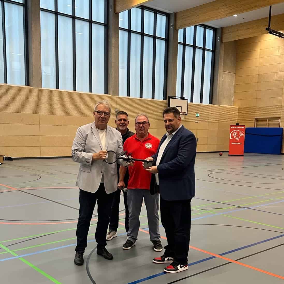 Vier Männer halten in der neuen Sporthalle gemeinsam einen übergroßen symbolischen Schlüssel.