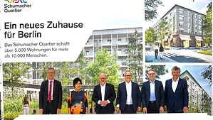 Sechs Personen mit Spaten und Bauhelmen stehen auf einer Sandfläche beim ersten Spatenstich.