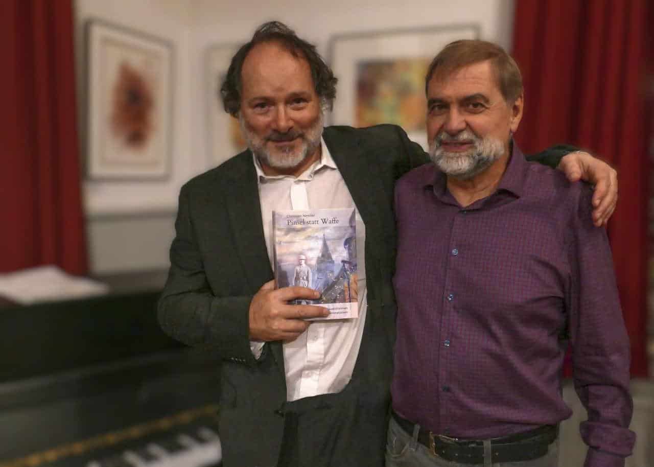Zwei Männer stehen nebeneinander, einer hält ein Buch in den Händen