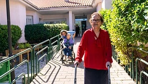 Ältere Frau mit Rollator wird im Freien von einer Begleitperson gestützt