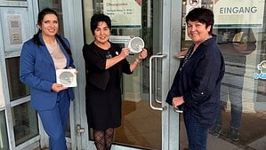 Drei Frauen halten am Glaseingang der Humboldt-Bibliothek runde Sticker mit Spiralmotiv