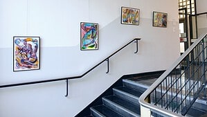 Treppenaufgang im Rathaus Reinickendorf mit gerahmten, farbenfrohen Gemälden an der weißen Wand und einem Metallgeländer.