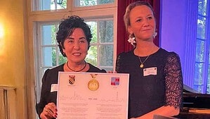 Zwei Frauen halten gemeinsam eine gerahmte Urkunde mit den Wappen von Reinickendorf und Antony und einer goldenen 60 in einem Saal mit Flügel.