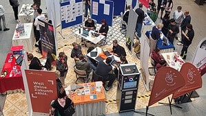 Blick von oben in eine Einkaufspassage mit Messeständen, Stellwänden und Tischen, an denen Jugendliche und Erwachsene im Gespräch sind.