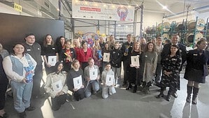 Gruppenfoto in einer Werkshalle mit Kabeltrommeln: Rund 30 Menschen, einige mit Urkunden und bunten Bären-Trophäen, stehen und knien vor einem Banner zur Verleihung des Reinickendorfer Ausbildungsbuddys
