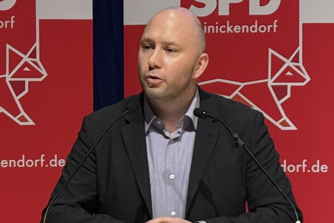 Alexander Ewers spricht an einem Redepult vor zwei Parteilogorollups der SPD Reinickendorf.