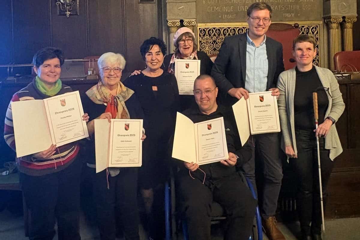 Sieben Personen stehen im BVV-Saal unter einer blau-goldenen Decke, fünf von ihnen halten Urkunden zum Ehrenpreis 2025.