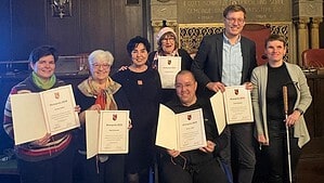 Sieben Personen stehen im BVV-Saal unter einer blau-goldenen Decke, fünf von ihnen halten Urkunden zum Ehrenpreis 2025.