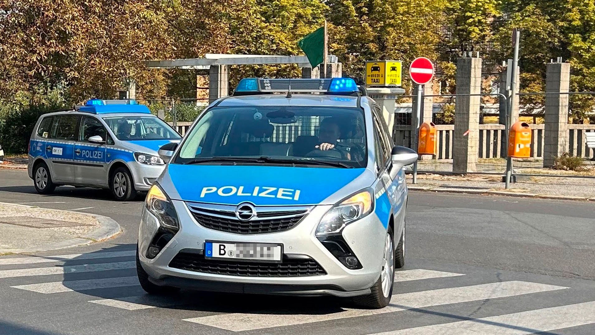 Ein Streifenwagen der Polizei Berlin mit eingeschaltetem Blaulicht fährt über einen Zebrastreifen, dahinter ein zweiter Streifenwagen.