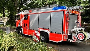 Ein rotes Löschfahrzeug der Berliner Feuerwehr mit Blaulicht steht an einer baumbestandenen Straße.