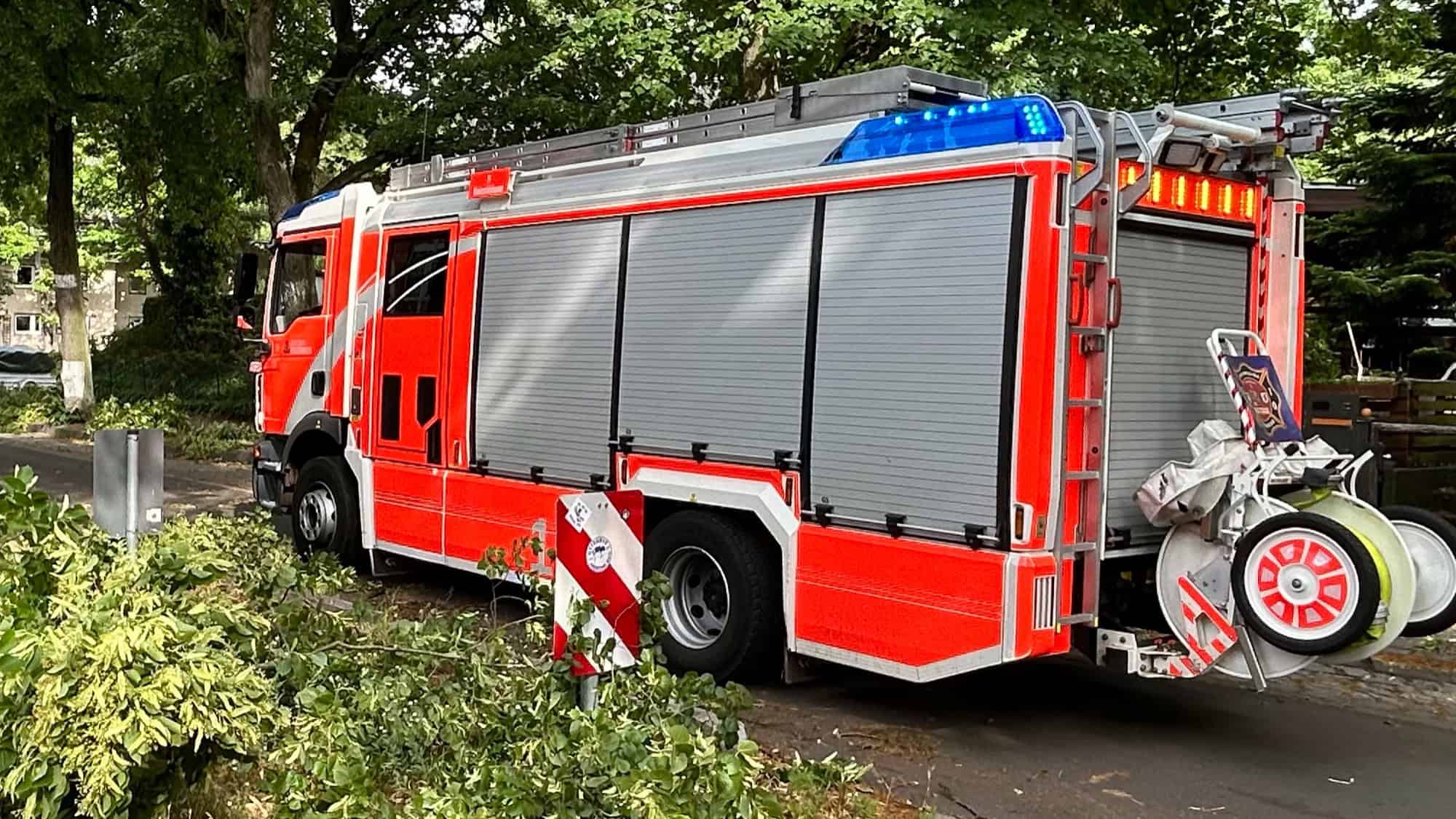 Ein rotes Löschfahrzeug der Berliner Feuerwehr mit Blaulicht steht an einer baumbestandenen Straße.